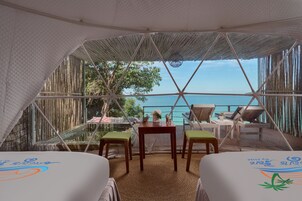 Habitación con tienda de campaña, dos camas, una mesa y sillas, con vista a una piscina y al mar.