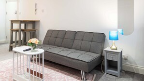 A modern living room with a grey sofa, a small white side table with a lamp, and a white side table with a vase of flowers.