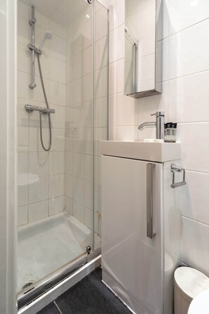 A modern bathroom with a glass-enclosed shower, a white sink with a mirror above it, and a toilet. - Chic Shoreditch Studio,Fast Wi-Fi & Top Location (London)