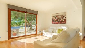 A modern living room with a white sofa, a glass sliding door leading to a garden, and a painting on the wall. - Villa Pancho - Large garden (Alcúdia)