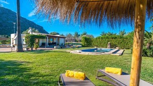 A pool area with lounge chairs and a thatched roof structure. - Villa Pancho - Large garden (Alcúdia)