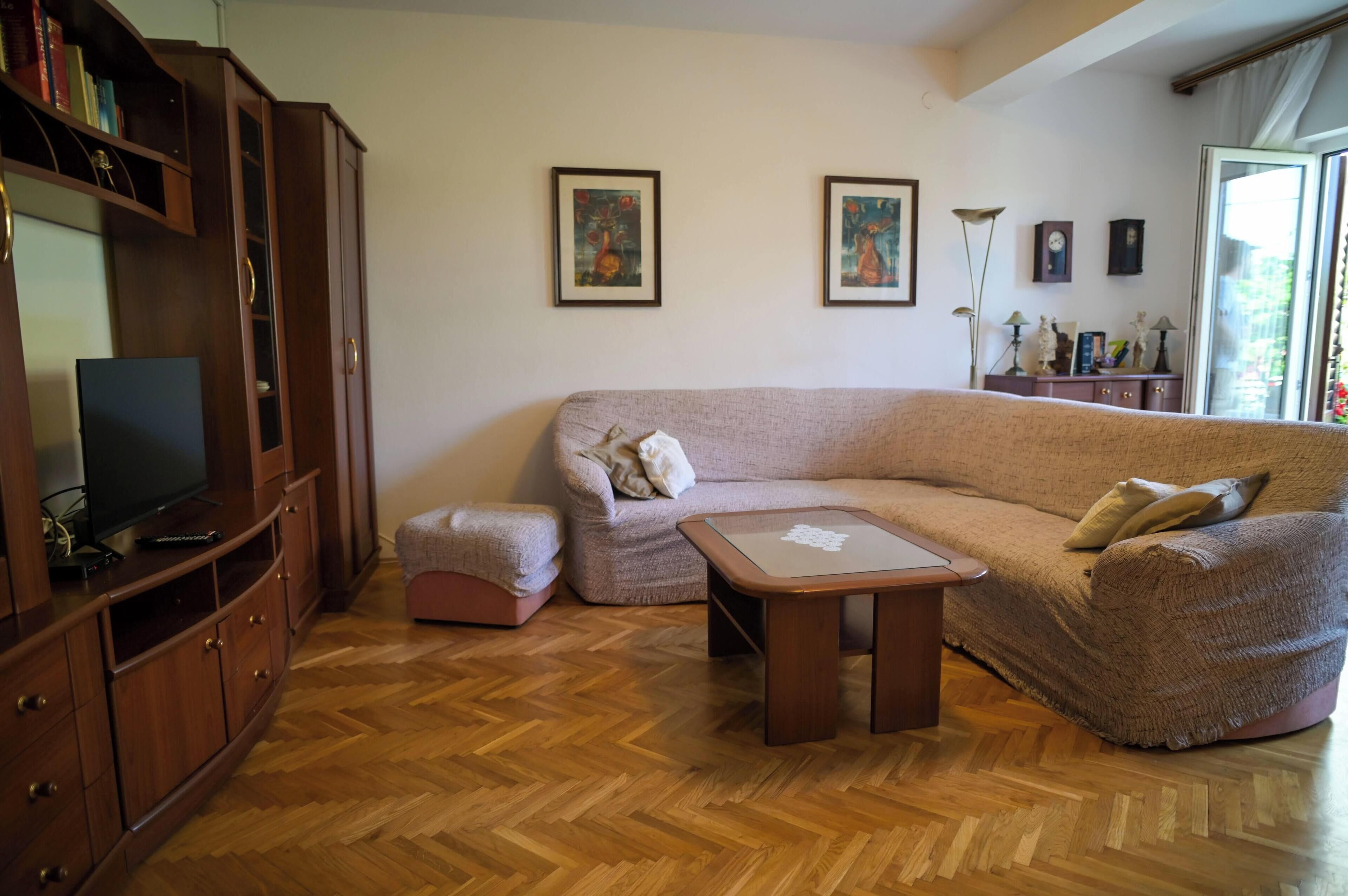 Un salon comprenant un canapé, un pouf, un meuble de rangement en bois et un téléviseur.