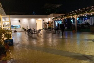 An outdoor patio area with tiled flooring, tables, chairs, and potted plants.