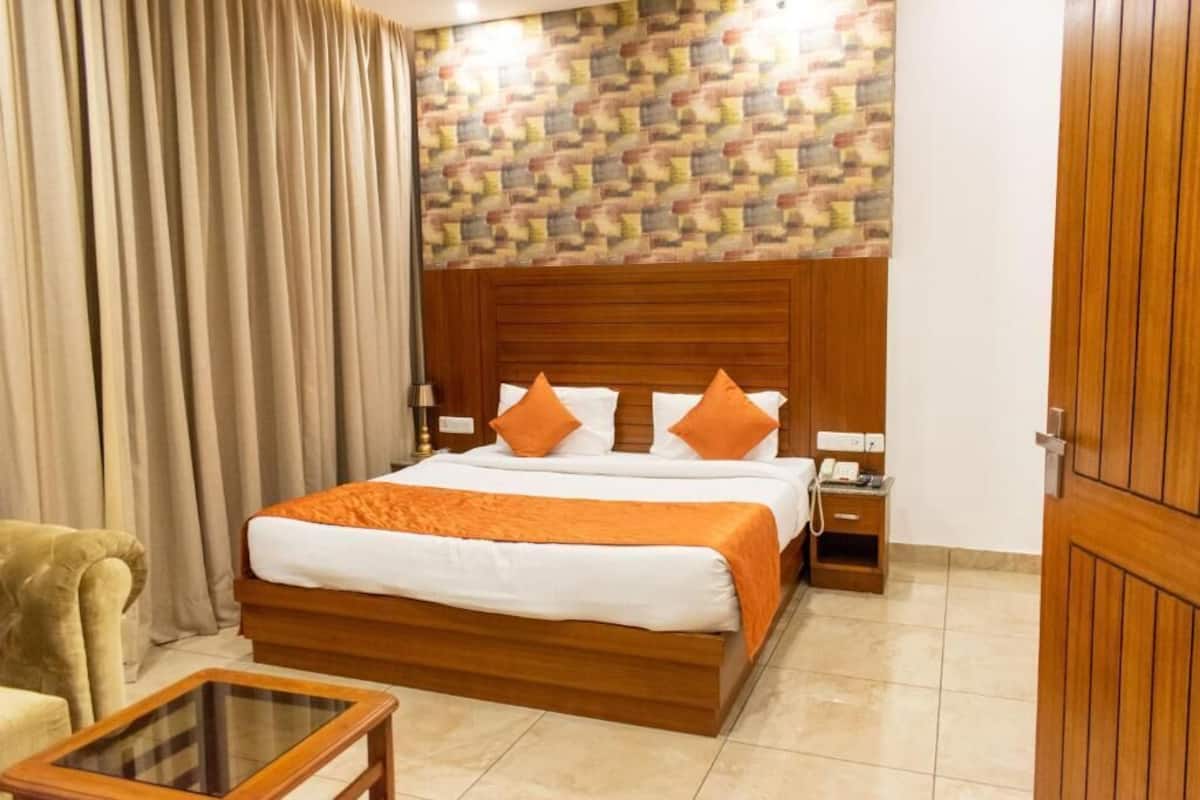 A hotel room with a wooden bed, orange bedding, a telephone, and a small bedside table.