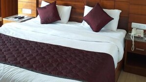 Een hotelkamer met een houten hoofdeinde, een bed met witte beddengoed en bordeauxrode kussens, een gewatteerde plaid en een telefoon op het nachtkastje.