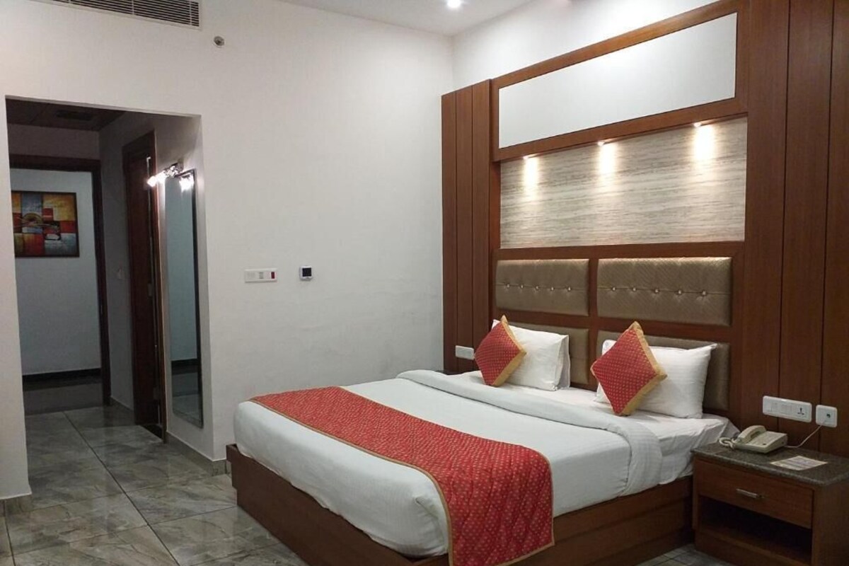 A hotel room with a large bed, a wooden headboard, a bedside table with a phone, and a red throw blanket.