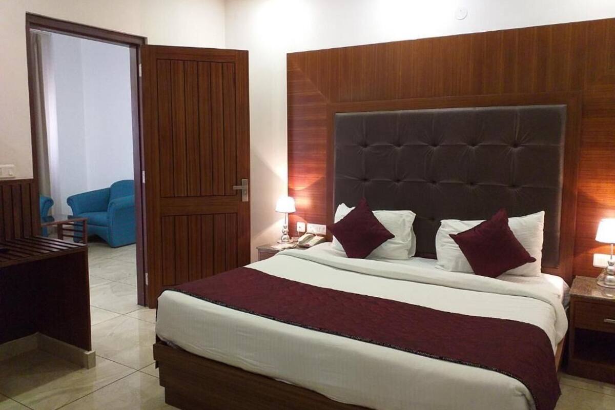 A hotel room with a large bed, wooden headboard, two bedside tables with lamps, a blue chair, and a wooden door.