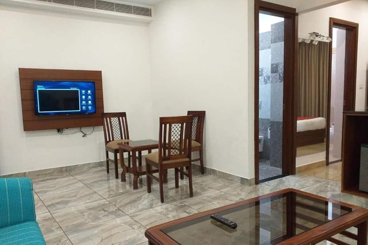 A living room with a sofa, a glass coffee table, a dining table with chairs, and a wall-mounted TV.