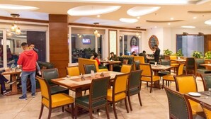 Een restaurant met meerdere tafels en stoelen, een televisiescherm op de achtergrond, en enkele gasten die dineren.