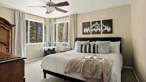 A bedroom with a bed, a ceiling fan, a window with curtains, and a wall with framed pictures.