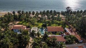 An aerial view of a resort with multiple buildings, a swimming pool, and a beach with palm trees. - Kalkudah Beach House (EP)