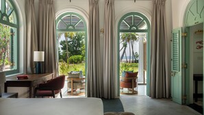A bedroom with a bed, desk, chair, and a view of the outdoors through arched windows. - Kalkudah Beach House (EP)