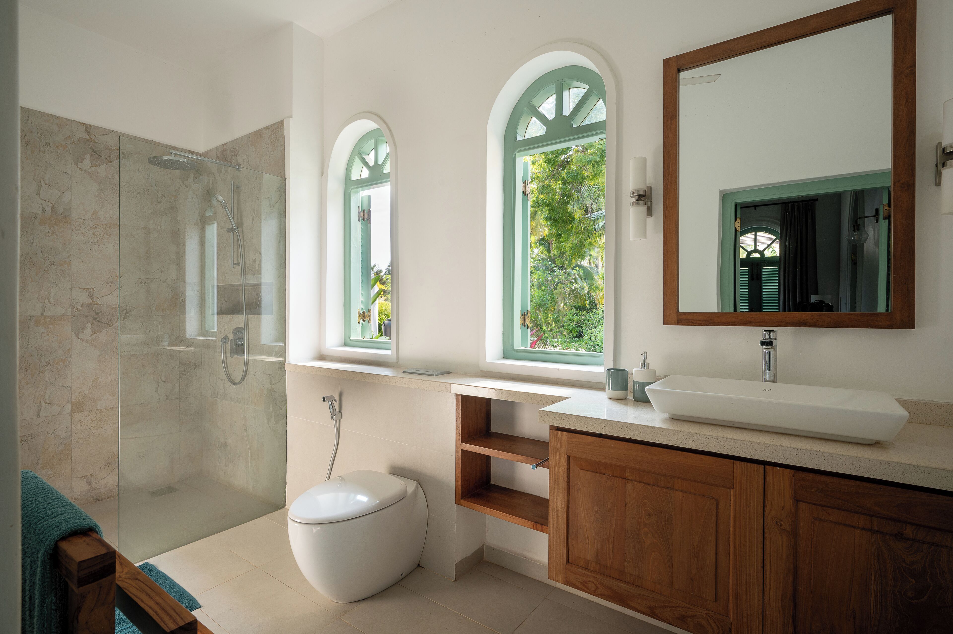 A modern bathroom with a glass-enclosed shower, a white toilet, a wooden vanity, and a large mirror.