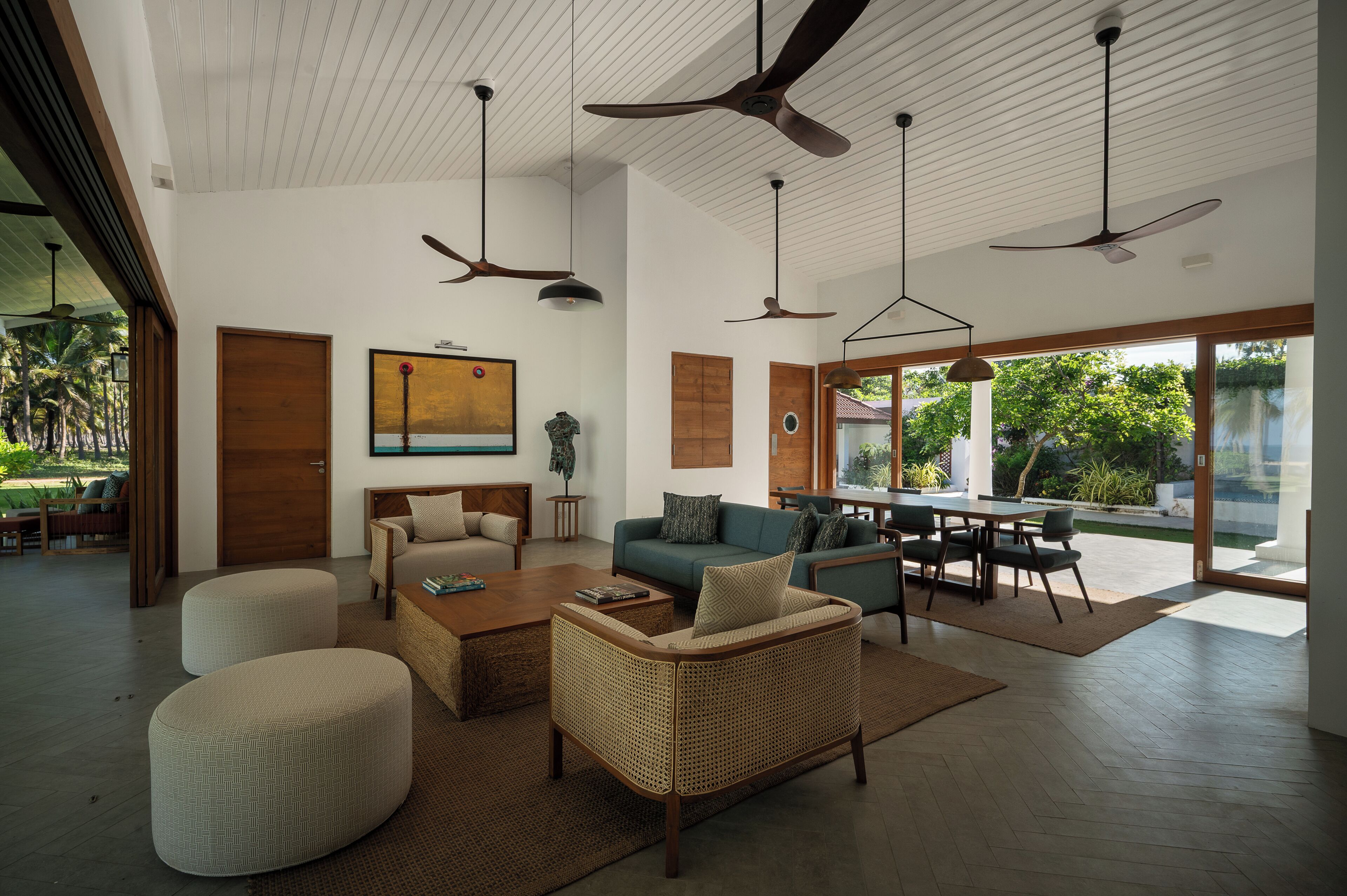 Amplia sala de estar con sofá, reposapiés y mesa de centro, una mesa de comedor con sillas y ventiladores de techo.