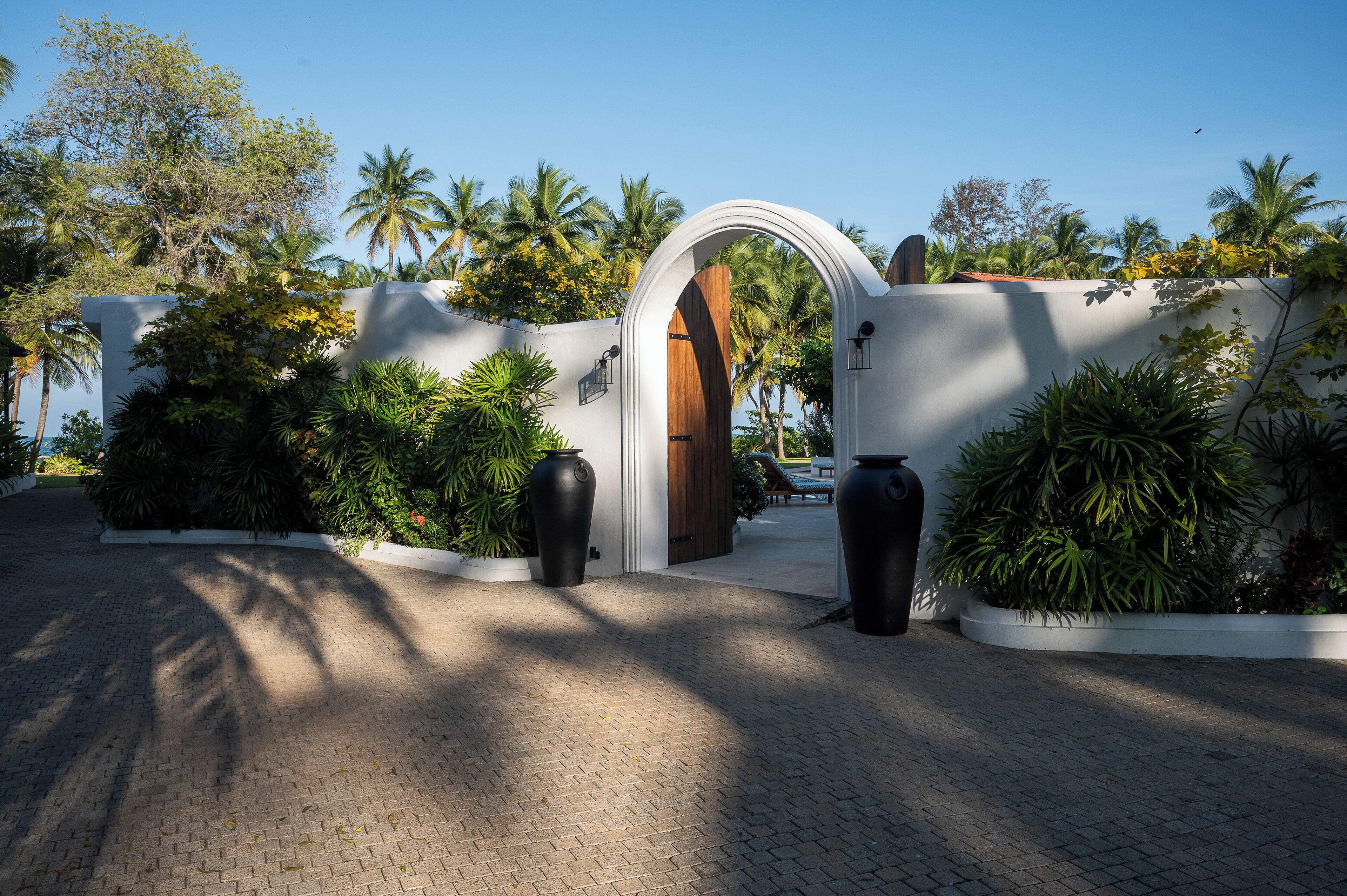 A gated entrance with a wooden door, surrounded by lush greenery and palm trees.