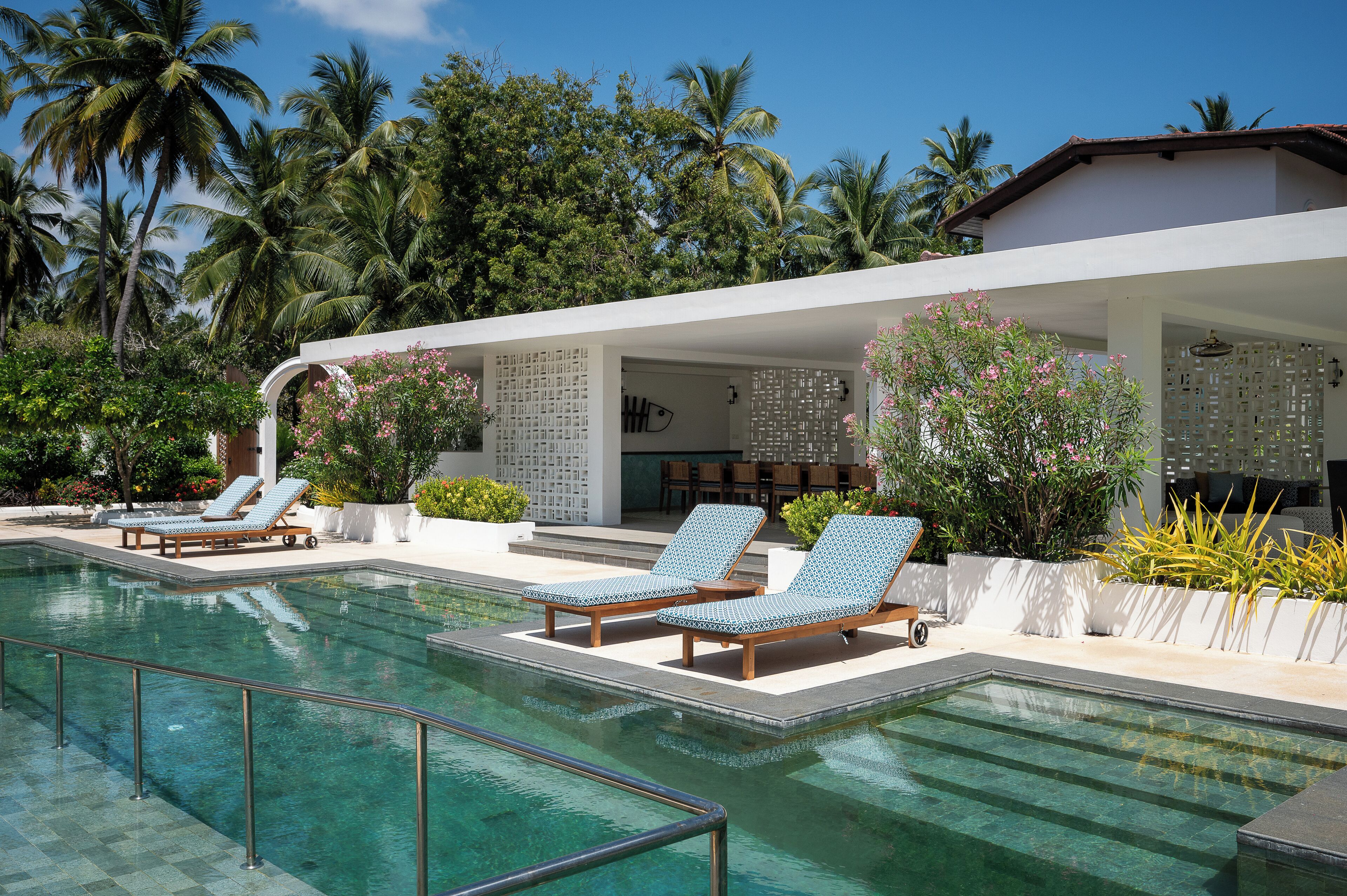 A pool area with lounge chairs and a covered seating area, surrounded by palm trees and greenery.