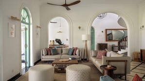 A spacious living room with a sofa, ottomans, a coffee table, and a ceiling fan. - Kalkudah Beach House (EP)