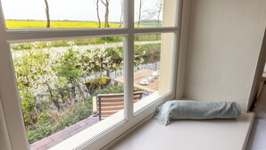 A room with a large window overlooking a garden and a table with chairs. - Lüsthuus vacation home - historic charm meets modern comfort (Krummhörn)