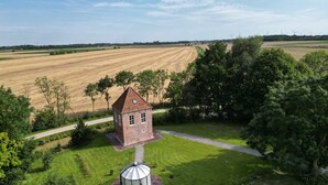 A small brick building with a tiled roof, surrounded by a well-maintained lawn and trees. - Lüsthuus vacation home - historic charm meets modern comfort (Krummhörn)
