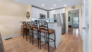 A modern kitchen with white cabinets, a stainless steel refrigerator, and a central island with bar stools. - Lighthouse Loft l Marshfront l Walk to Downtown (St. Augustine)