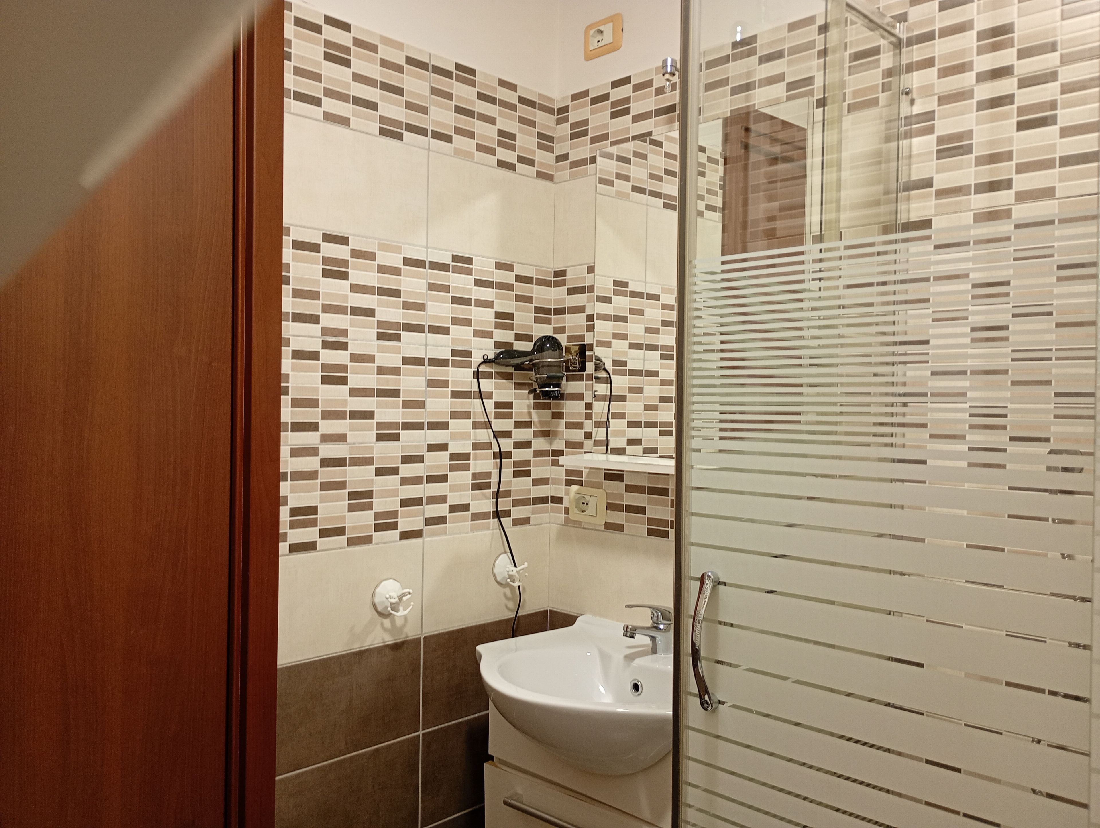 A bathroom with a tiled wall, a sink, and a shower area.