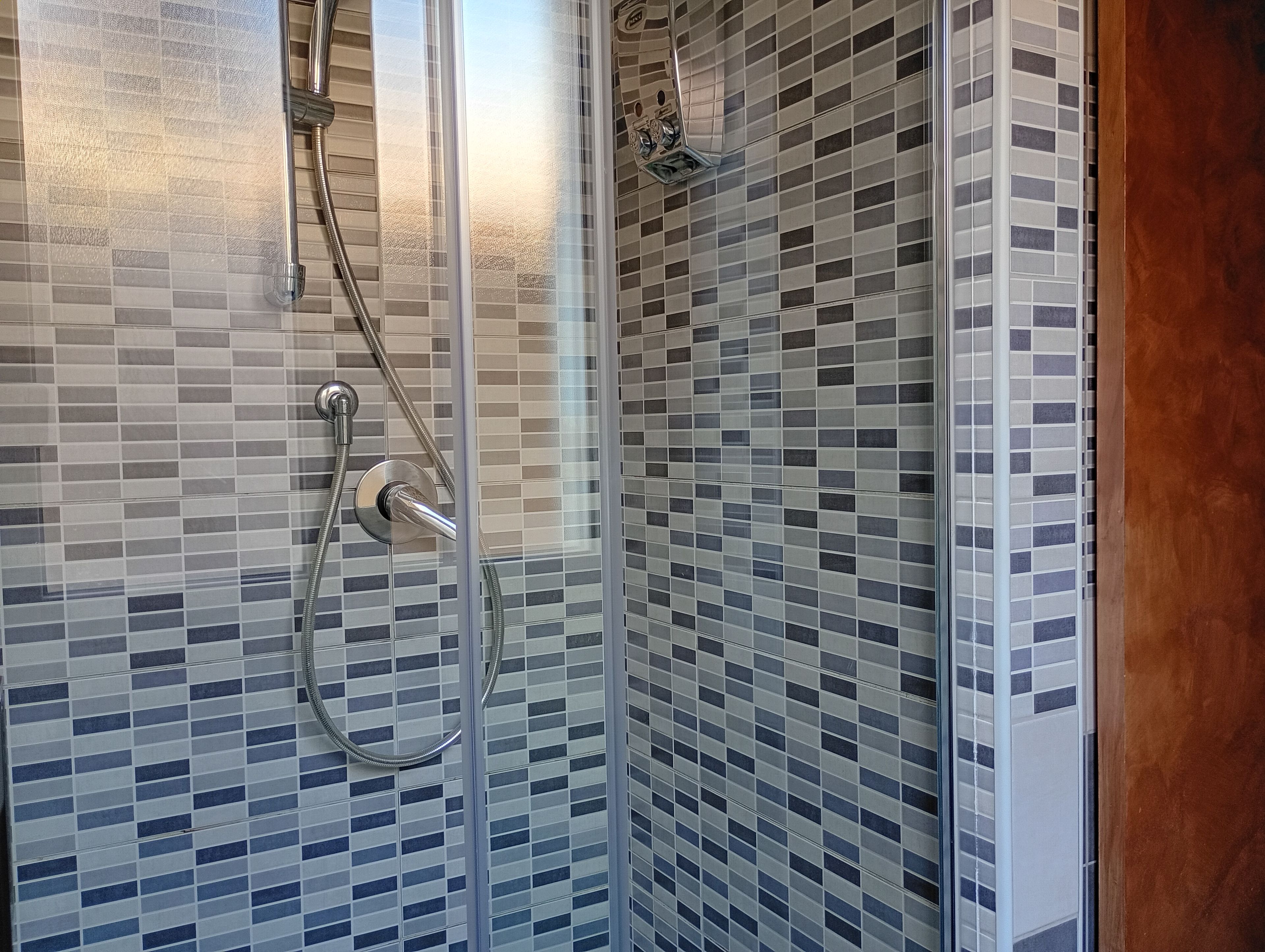A shower with a glass door and a tiled wall.