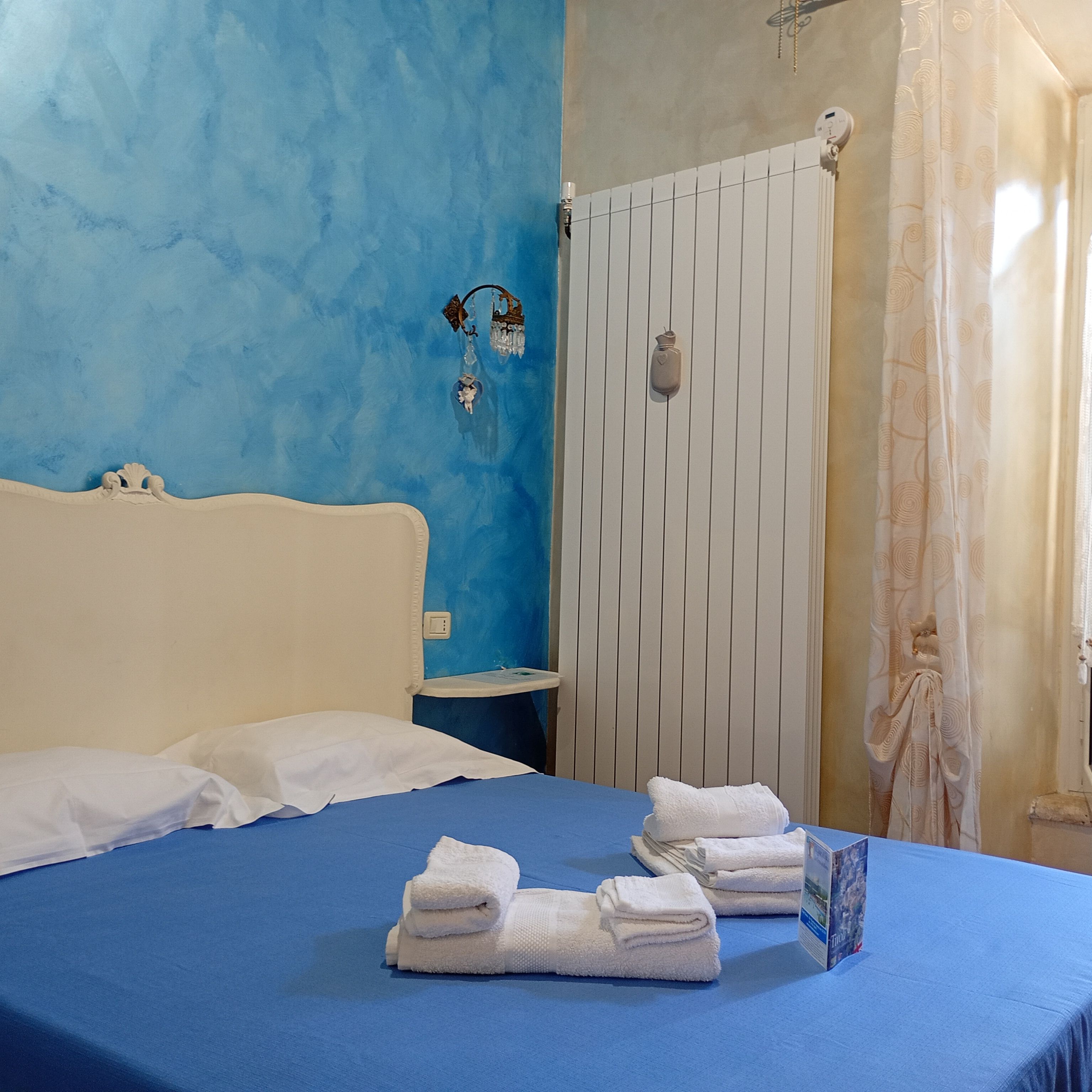 Une chambre d’hôtel avec un mur bleu, un lit blanc et une salle de bain avec un rideau de douche blanc.