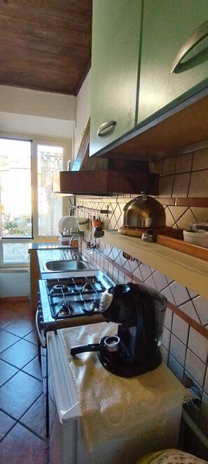 A kitchen with a gas stove, a coffee maker, and a window with a view of the outside. - La Mensa Ponderaria (Tivoli)