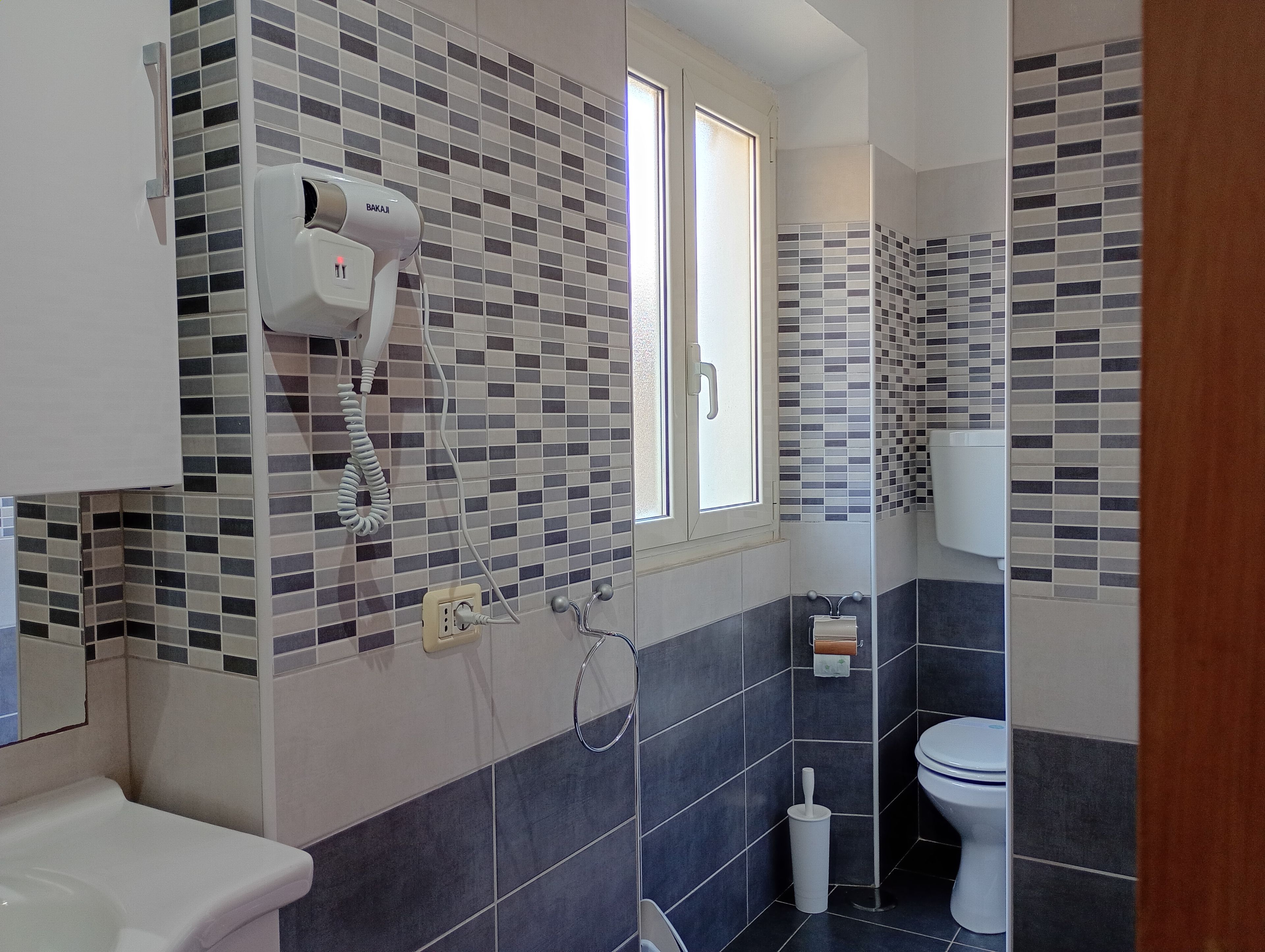 A bathroom with a tiled wall, a white toilet, a hand dryer, and a window.