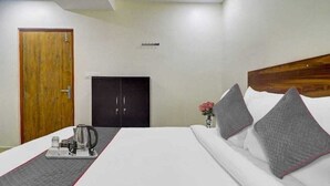 Une chambre d’hôtel avec un lit, une porte en bois, une armoire et une petite table sur laquelle se trouvent une bouilloire et des tasses.