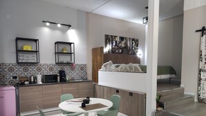 Eine kompakte Küche mit Mikrowelle, Toaster und Wasserkocher, ein Essbereich mit Tisch und Stühlen sowie ein Etagenbett mit einer grünen Tagesdecke.