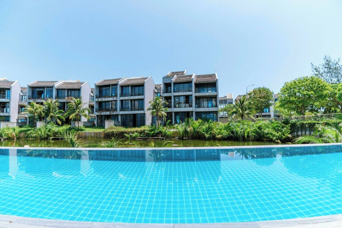 A swimming pool with tiled blue water, surrounded by greenery and modern buildings with balconies.