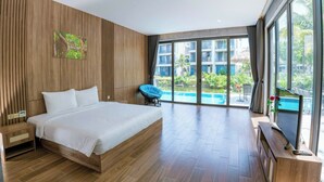A modern hotel room with a large bed, wooden panel walls, a painting, a view of a swimming pool, and a TV on a wooden console. - Gold Riverside Apartment & Villa (Da Nang)