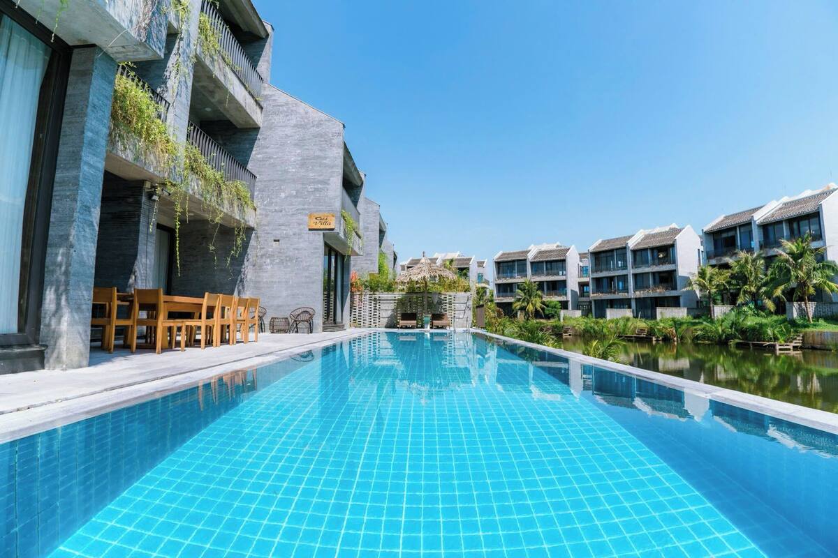 A swimming pool with tiled blue water, surrounded by modern buildings with balconies and outdoor seating.