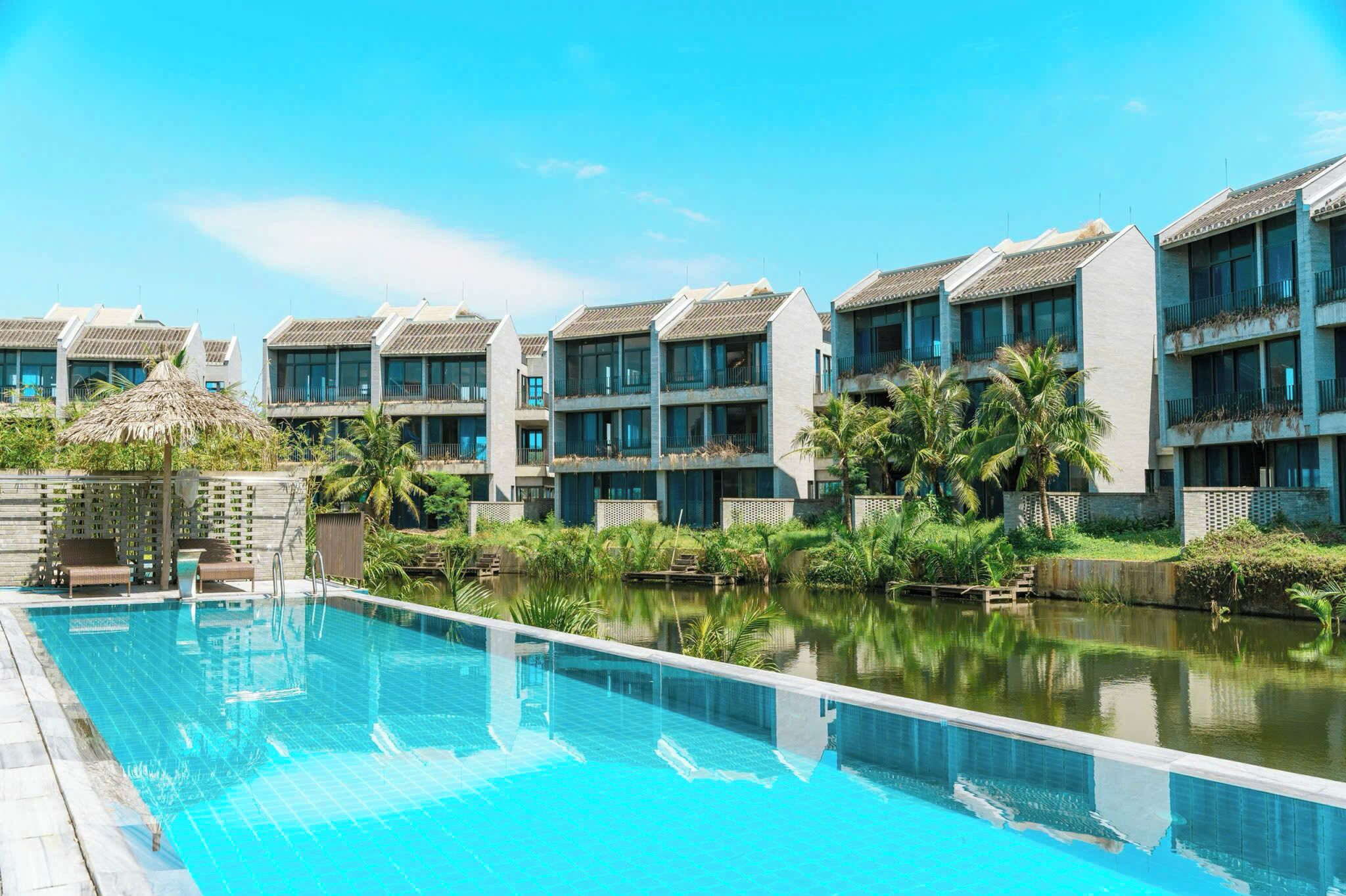 A modern hotel with a swimming pool, multiple balconies, and lush greenery.