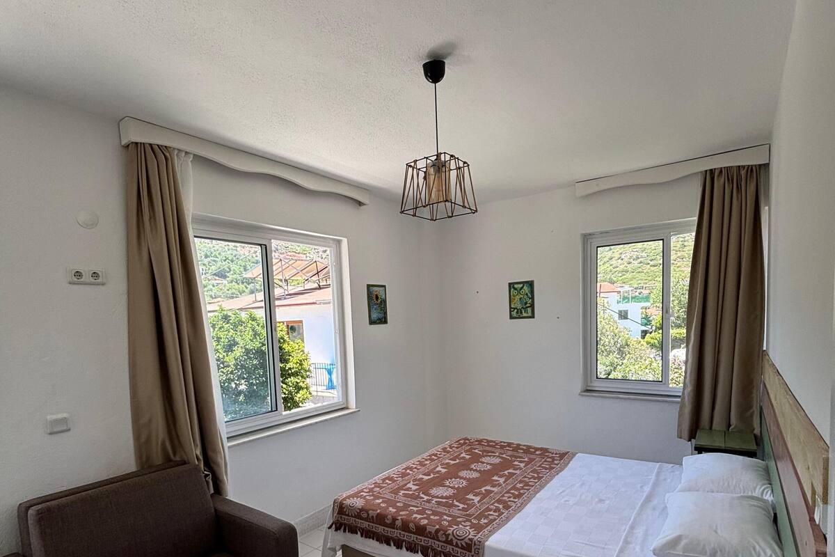 A bedroom with a bed, a sofa, a small table, and two windows with curtains.