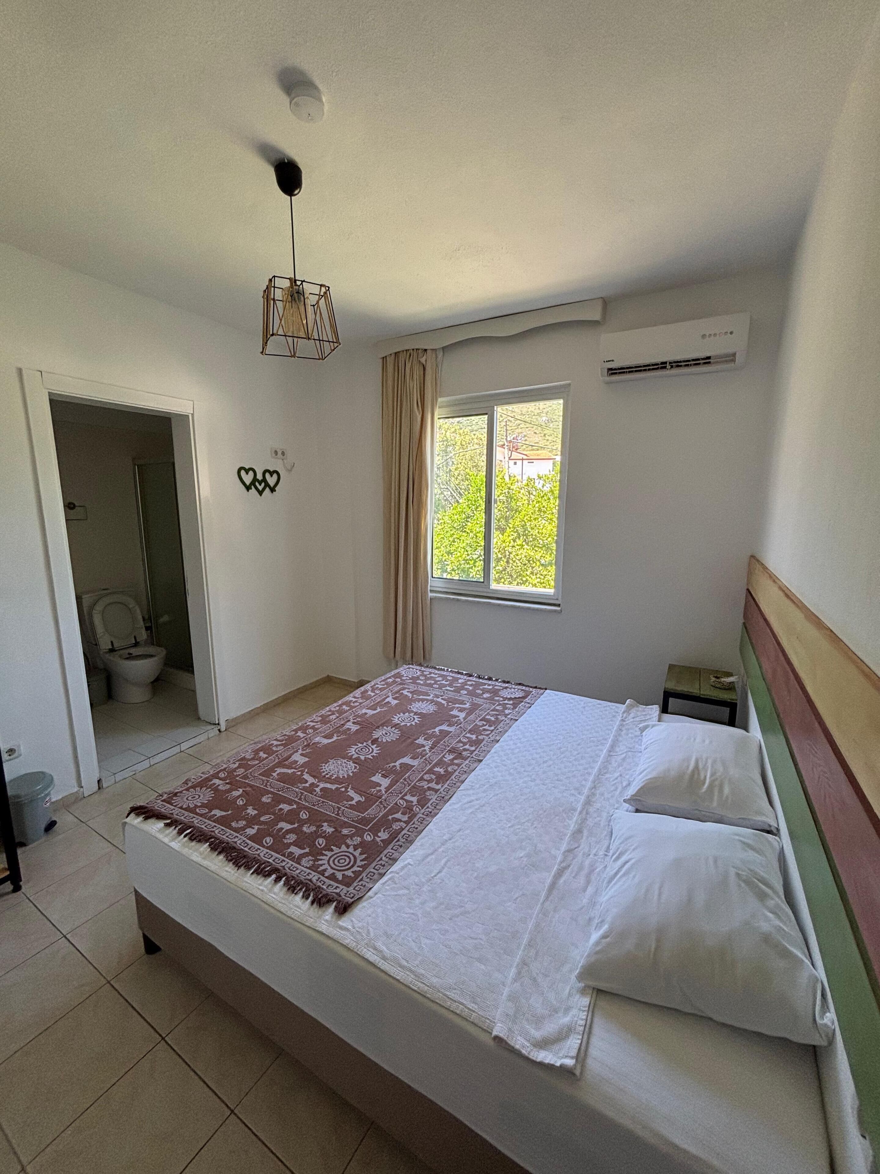 A bedroom with a bed, a window, an air conditioning unit, and a ceiling fan.