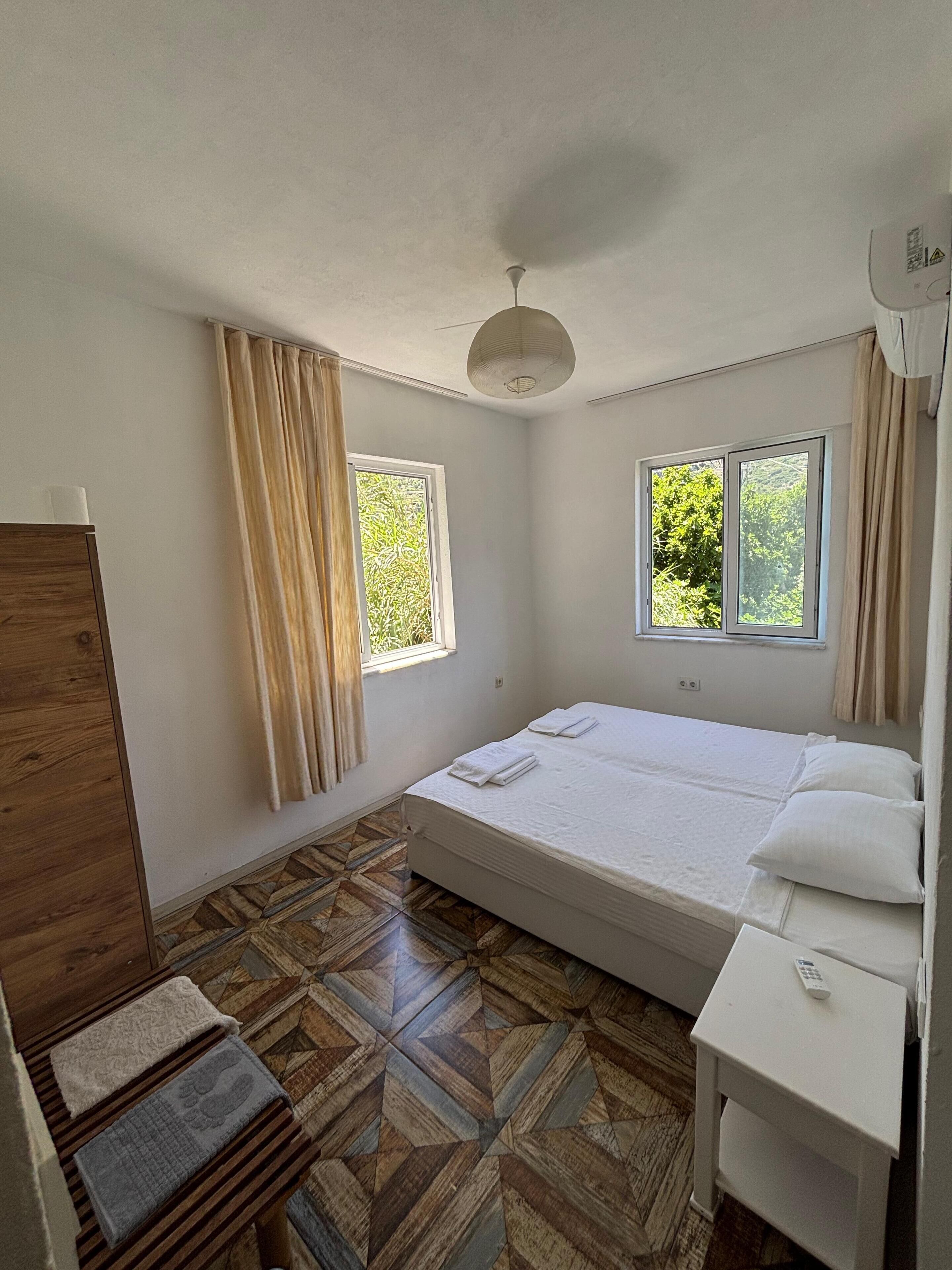 A room with a bed, two windows, a ceiling fan, and a wooden wardrobe.