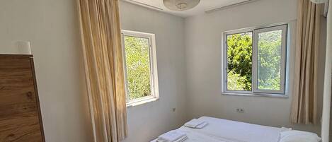 A room with a bed, two windows, a ceiling fan, and a wooden wardrobe.