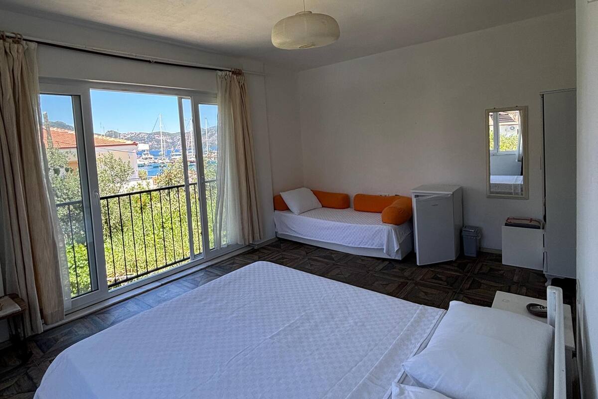 A hotel room with a large bed, a small desk, a refrigerator, and a balcony with a view of the city.
