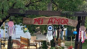 Ein rustikaler Außenbereich mit Sitzgelegenheiten und einem hölzernen Bogen, der "MJ AMOR" zeigt, mit daran hängenden Traumfängern.