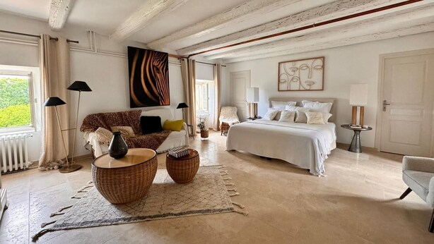 Un dormitorio amplio con una cama grande, un área de descanso con sofá y sillones, y vistas a zonas verdes.