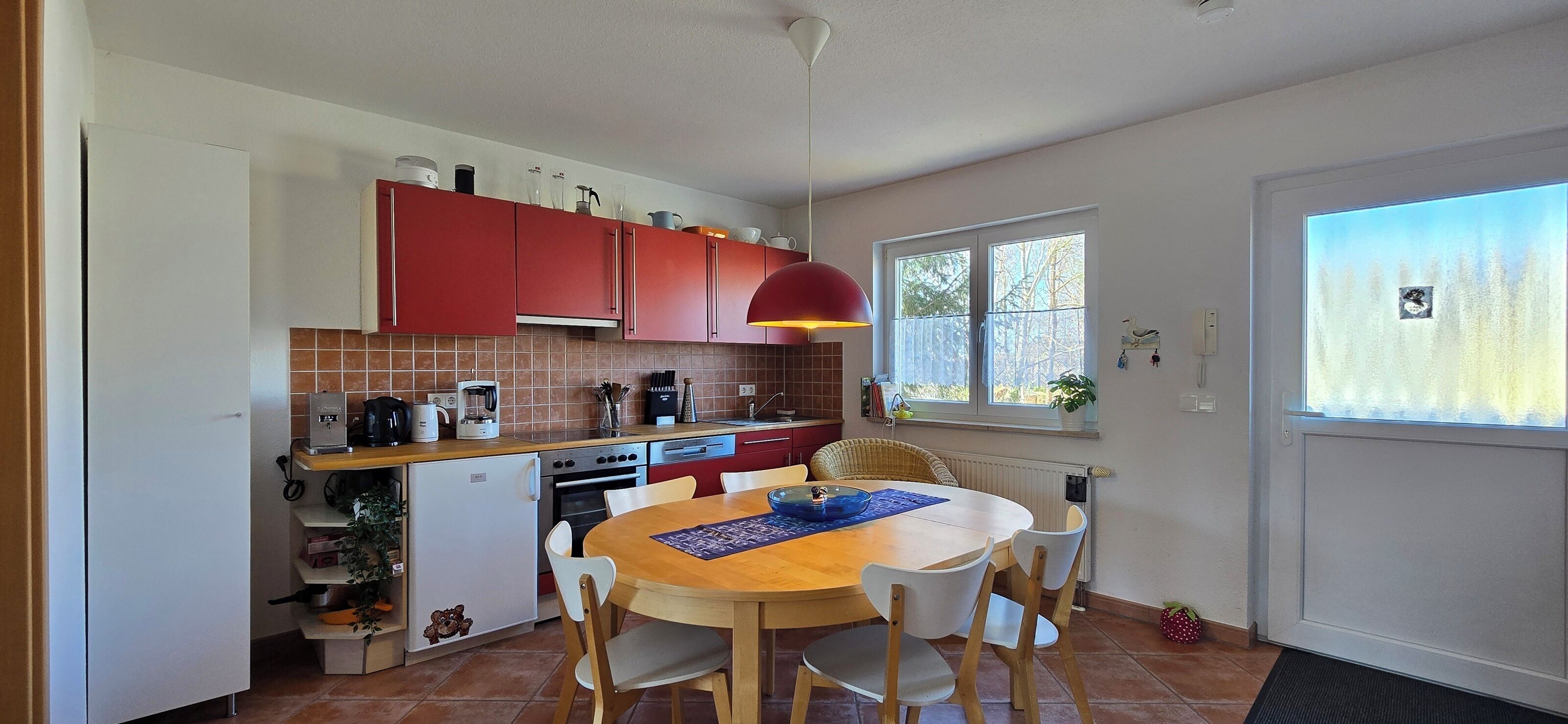 A compact kitchen with red cabinets, a dining table with chairs, and a window providing natural light.