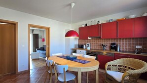 Une cuisine moderne avec des meubles de rangement rouges, une table à manger en bois et une chaise en osier.