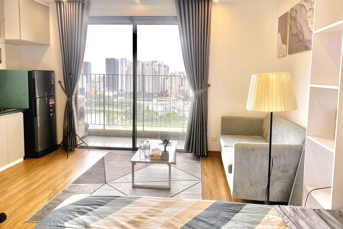 A modern hotel room with a city view, a kitchenette, a sofa, a lamp, and a coffee table.