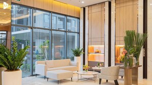 A modern lobby with a sofa, armchair, and coffee table, large windows, and indoor plants.