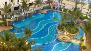 A large indoor swimming pool with multiple levels and water features, surrounded by palm trees and outdoor seating areas.