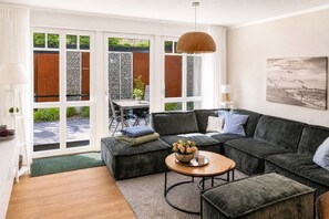 A modern living room with a sectional sofa, a coffee table, and a large window with a view of greenery. - Beach shell vacation apartment at Villa Beatrice - your retreat in Binz (Binz)
