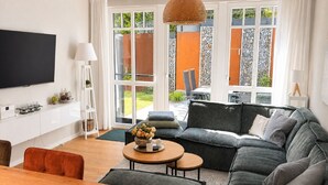 A modern living room with a large flat-screen TV, a grey sofa, a wooden coffee table, and a dining area with a wooden table and chairs. - Beach shell vacation apartment at Villa Beatrice - your retreat in Binz (Binz)