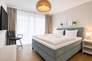 A modern hotel room with a large bed, a TV, a chair, and a bedside table with a lamp. - Beach shell vacation apartment at Villa Beatrice - your retreat in Binz (Binz)